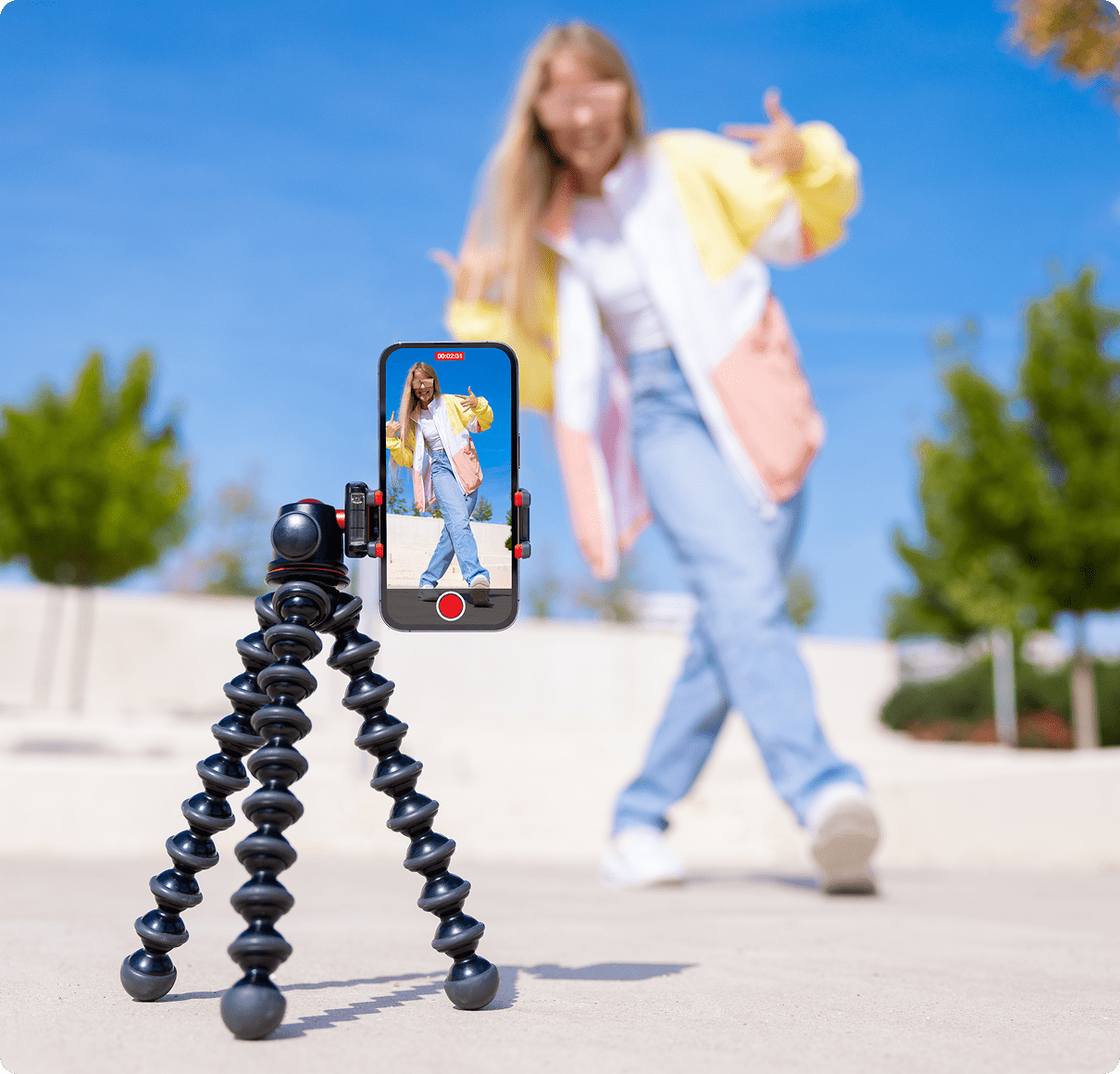 Phone on tripod filming woman outdoors dancing.